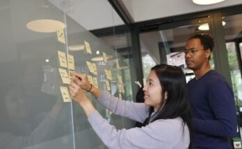 Two individuals writing on sticky notes on a glass wall, collaborating on knowledge management strategies.
